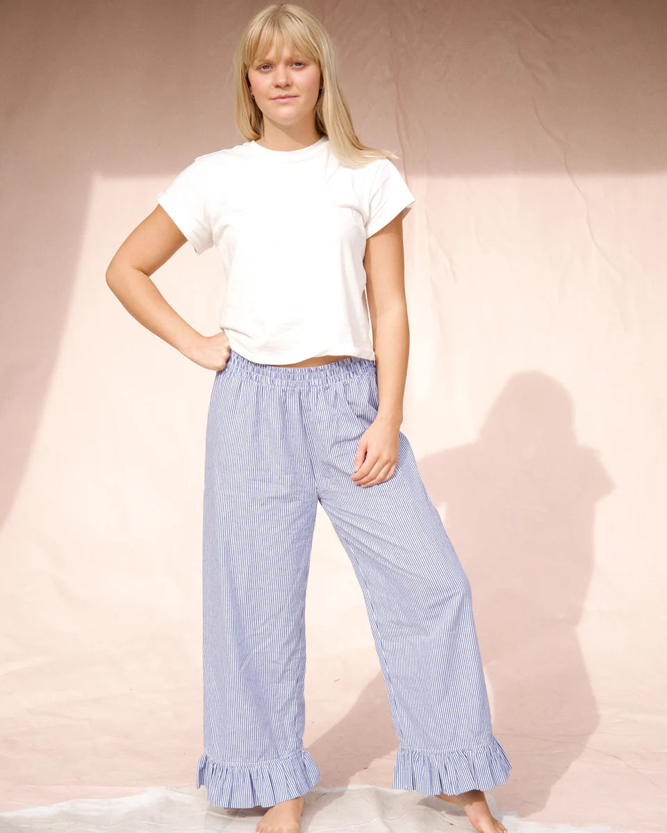 Woman wearing a white t-shirt and light blue ruffled pants against a plain background