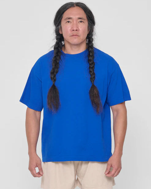 Person wearing a blue t-shirt and beige shorts with long braided hair on a white background