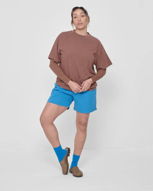 Person wearing a brown top and blue shorts with blue socks on a white background