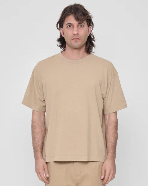 Man wearing a beige t-shirt and pants against a white background