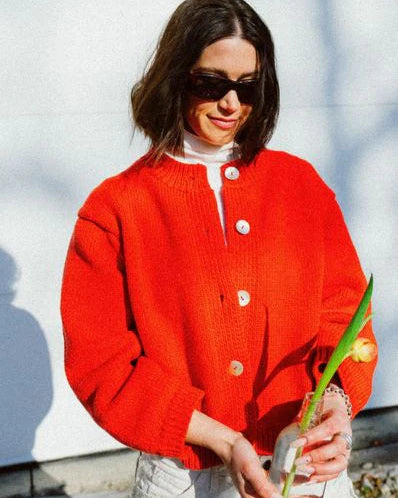 Woman wearing a red cardigan holding a plant against a light background