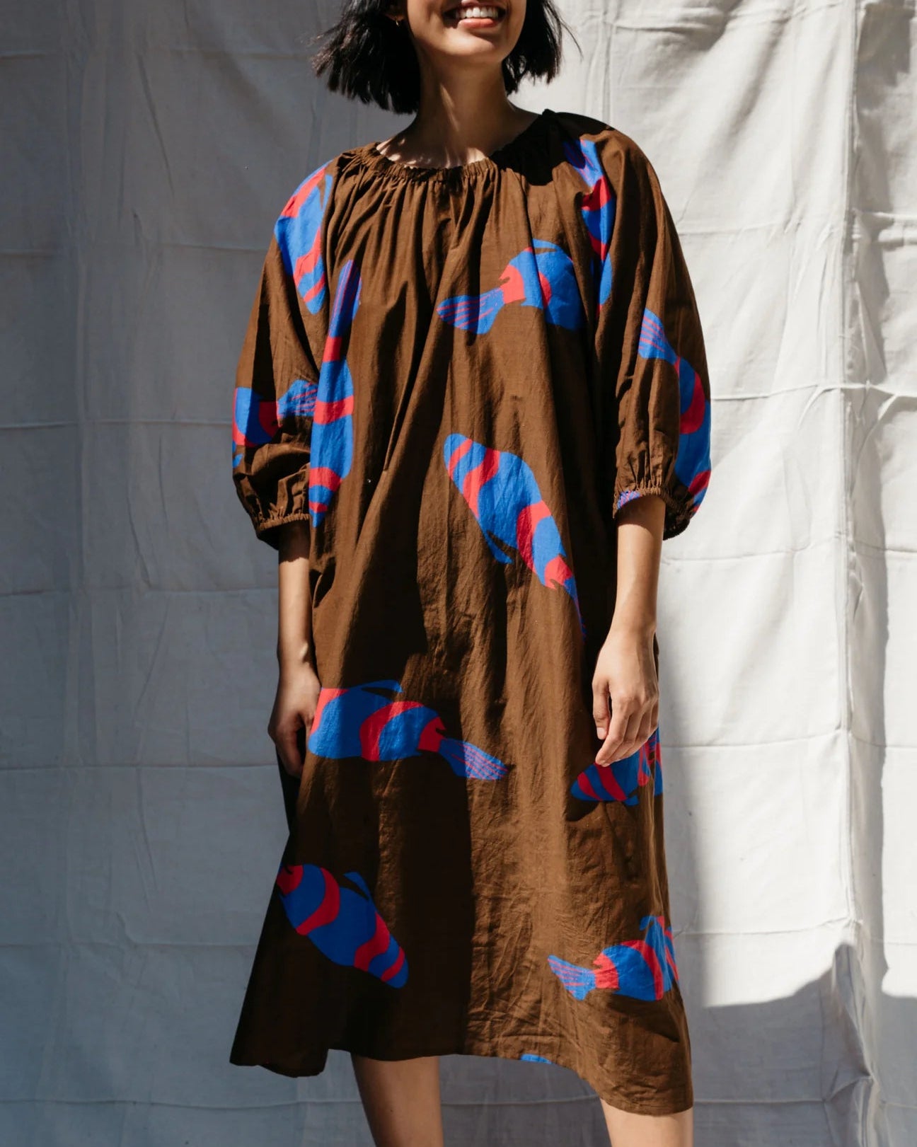 Woman wearing a brown dress with blue and red patterns against a white backdrop