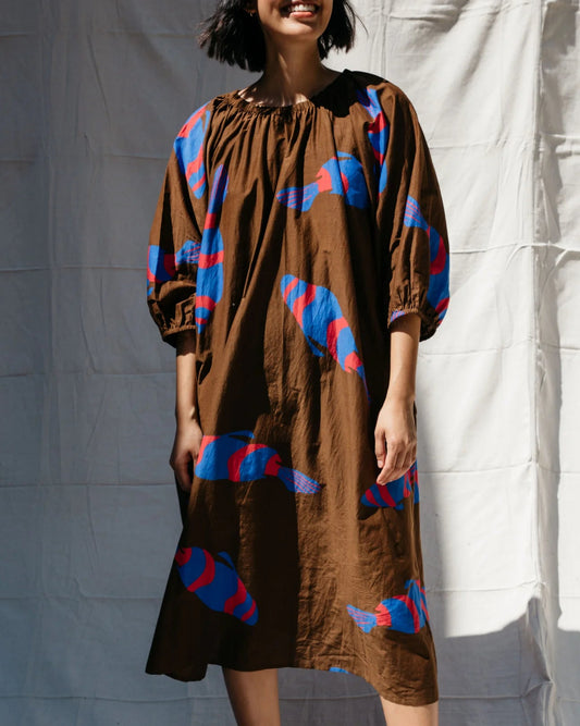 Woman wearing a brown dress with blue and red patterns against a white backdrop