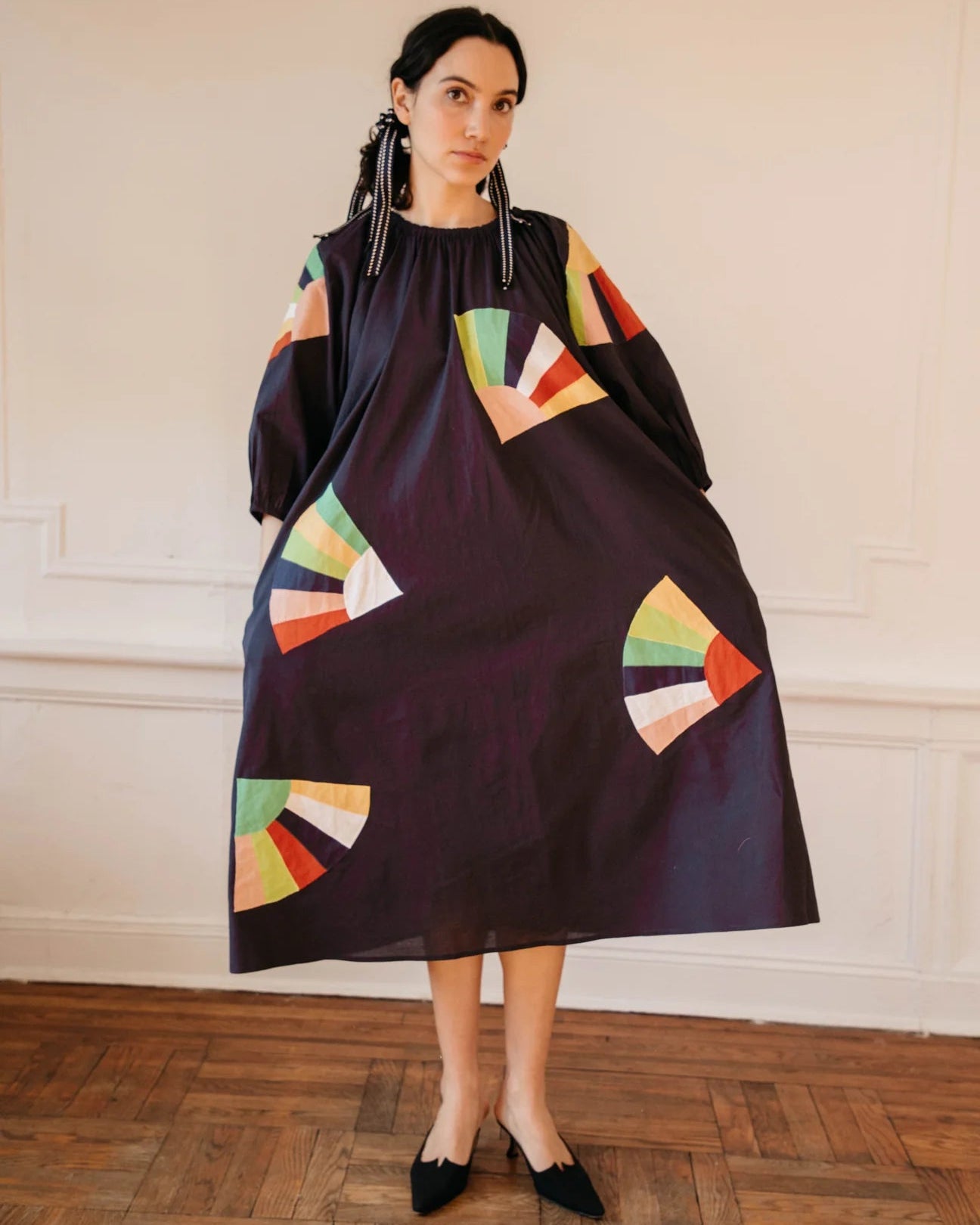 Woman wearing a black dress with colorful geometric patterns in an indoor setting.