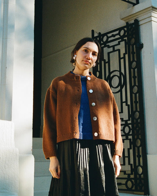 Woman wearing a brown cardigan over a blue top and black skirt, standing in front of a decorative gate.