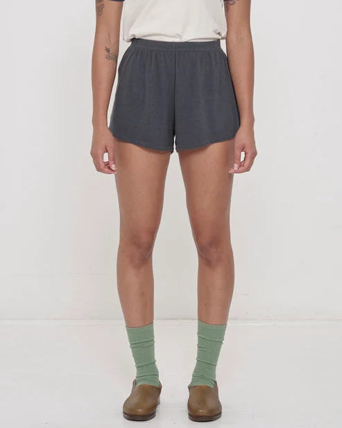 Person wearing gray shorts, green socks, and brown shoes on a white background