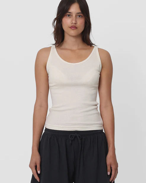 Woman wearing a beige tank top and black pants on a white background