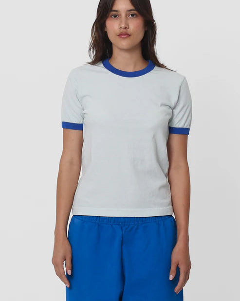 Woman wearing a white t-shirt with blue trim and blue pants on a light gray background