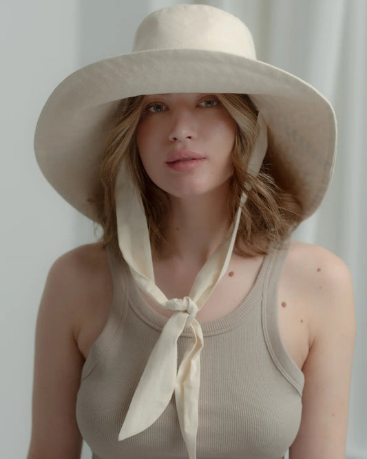 Woman wearing a beige sun hat with a scarf, standing against a plain background