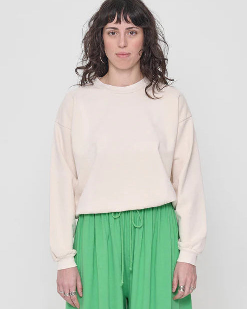 Woman wearing a cream sweater and green pants against a white background