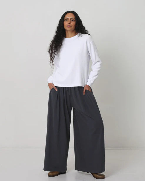 Person wearing a white sweater and dark gray wide-leg pants on a white background