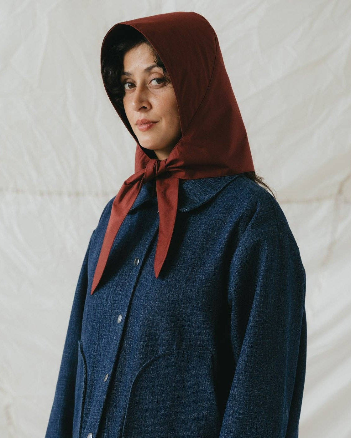 Person wearing a blue coat and red hooded scarf against a neutral background