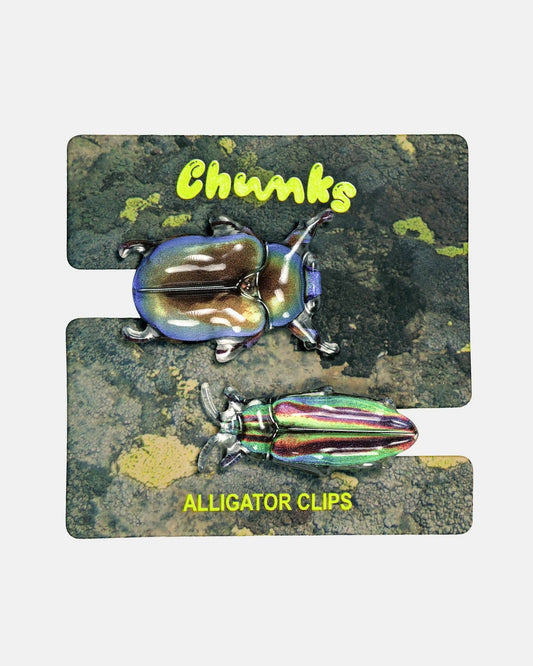 A pair of iridescent alligator-style clips displayed on a printed backing card. The backing card has a dark textured background with two beetle illustrations and yellow text reading 'Chunks' and 'ALLIGATOR CLIPS'.