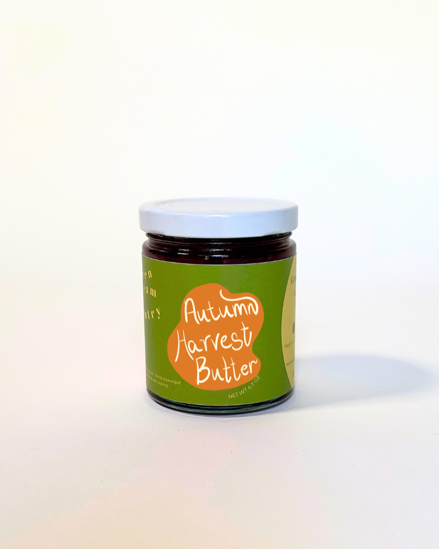A small glass jar of autumn harvest butter with a green and orange label, set against a plain white background.