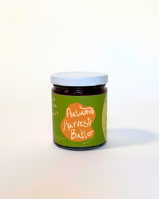 A small glass jar of autumn harvest butter with a green and orange label, set against a plain white background.