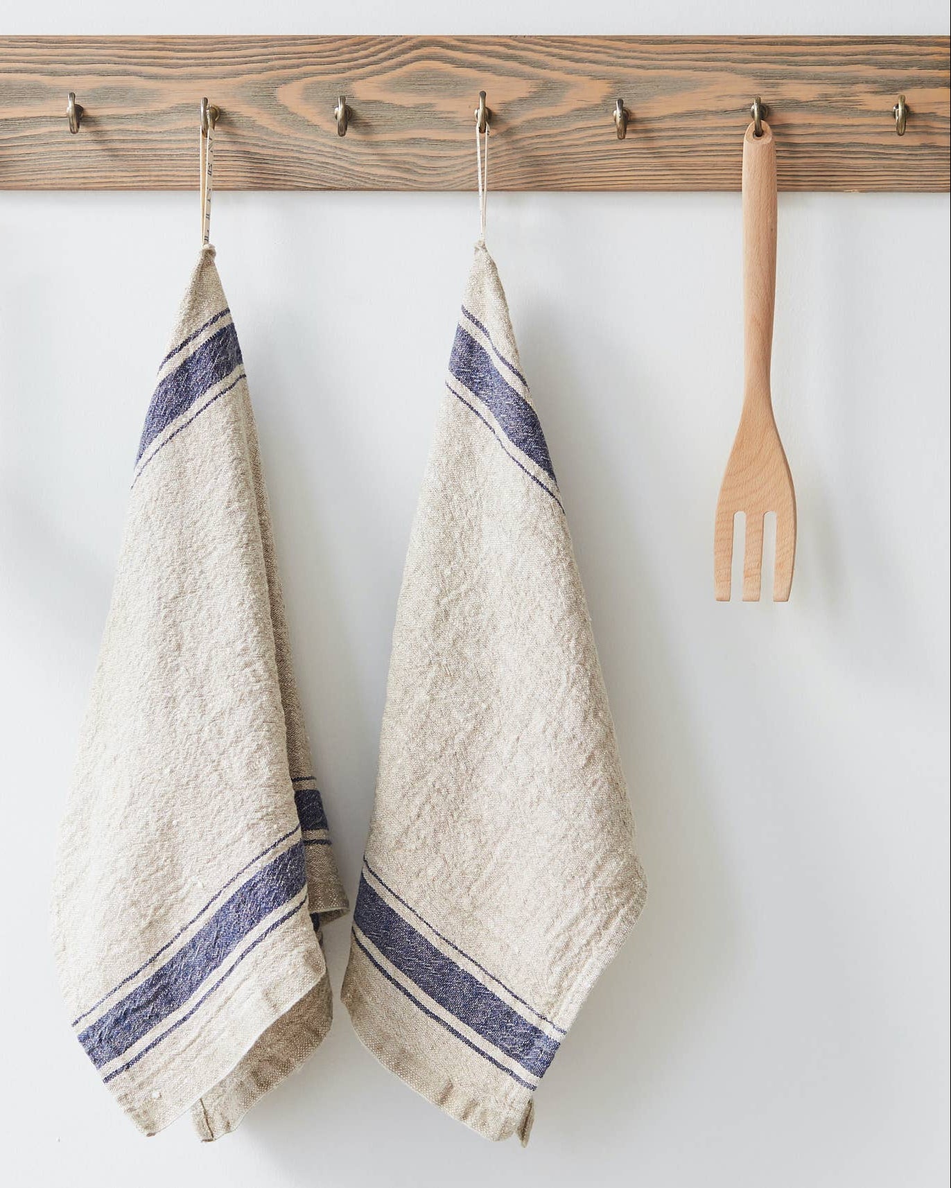 Two beige towels with blue stripes hanging on a wooden rack with kitchen utensils.