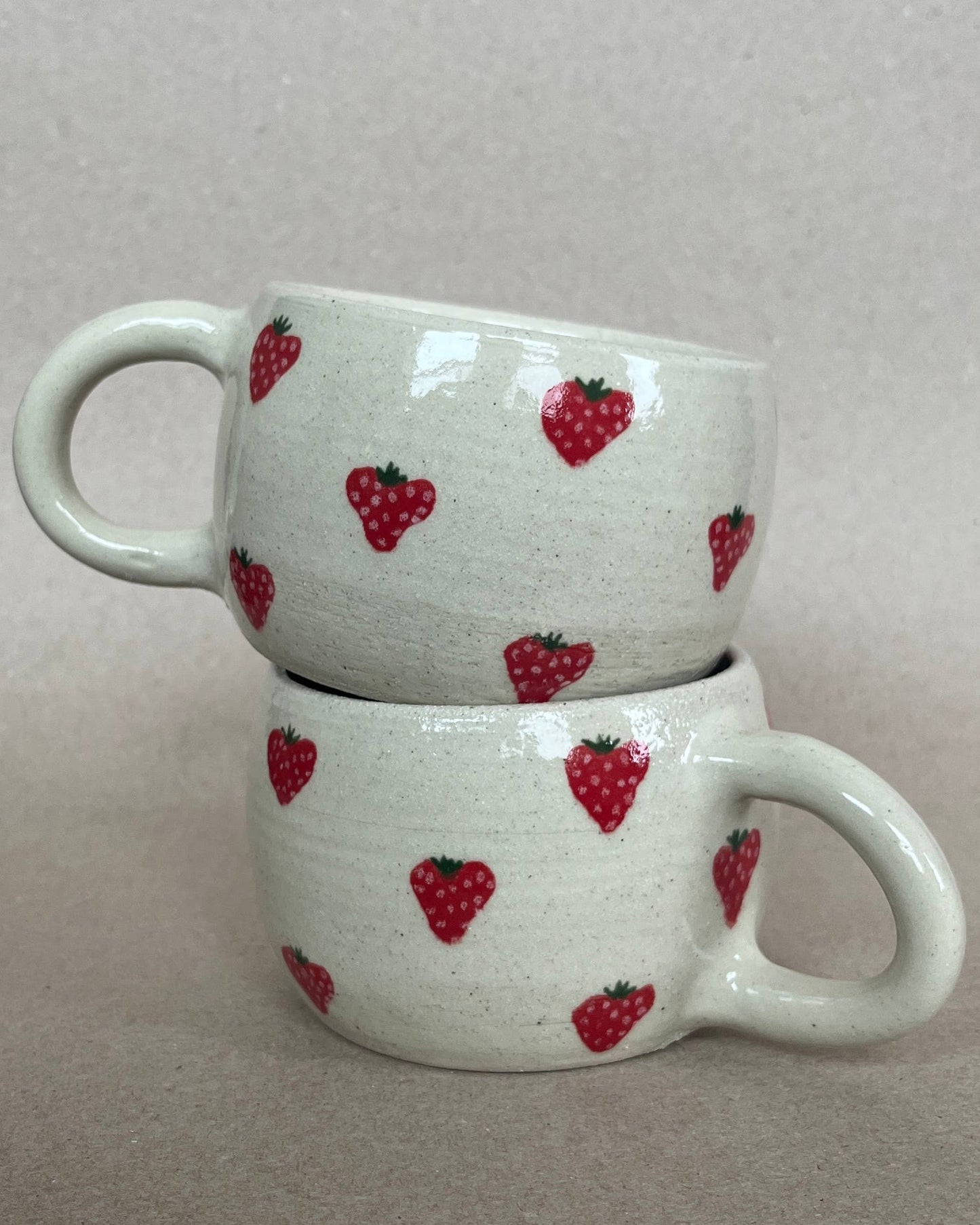 Two stacked ceramic mugs with strawberry pattern on a plain background