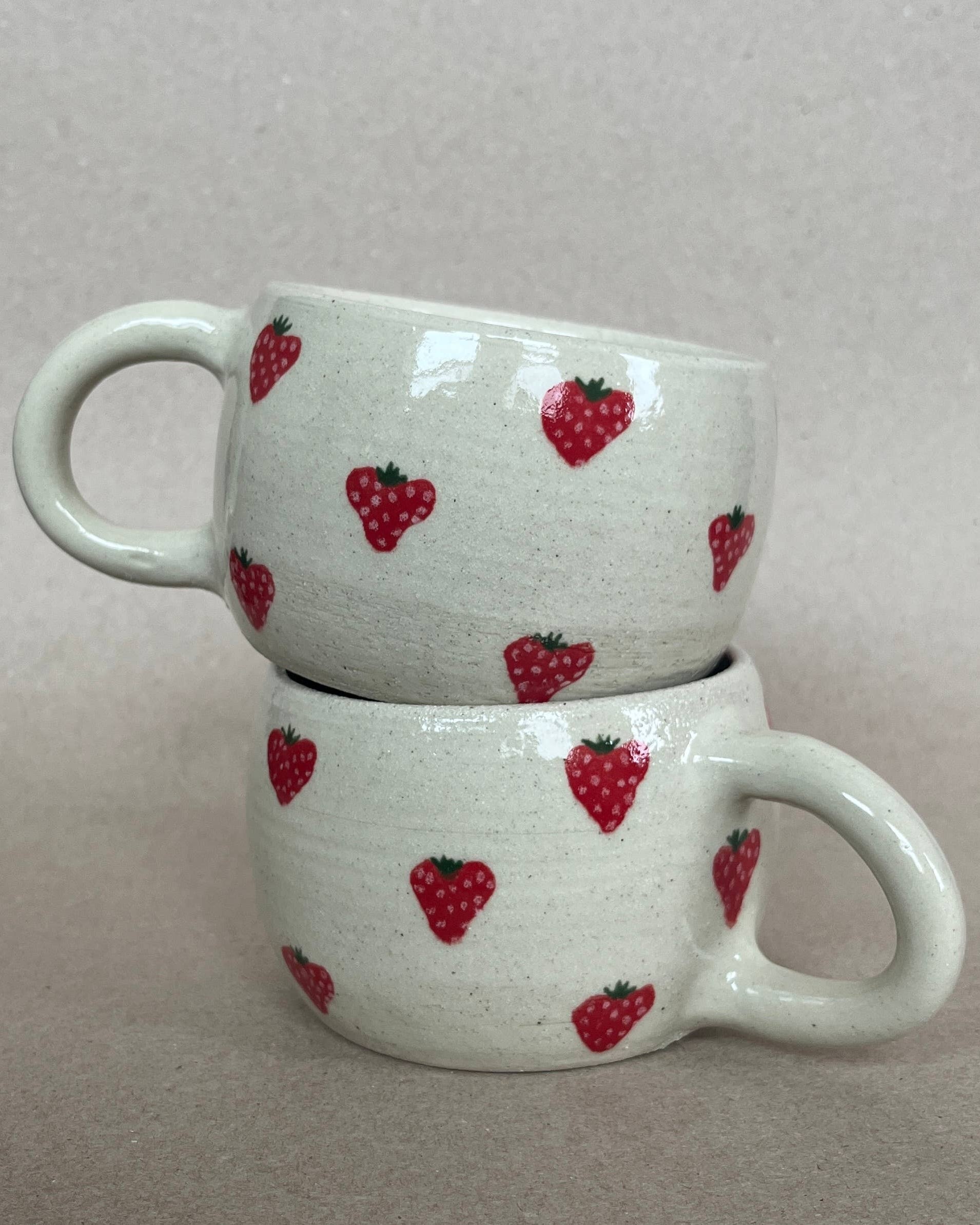 Two stacked ceramic mugs with strawberry pattern on a plain background