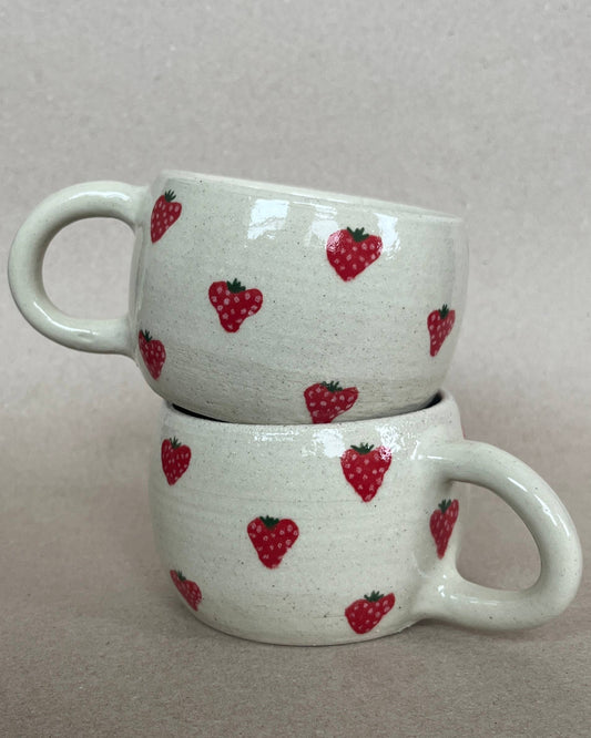 Two stacked ceramic mugs with strawberry pattern on a plain background