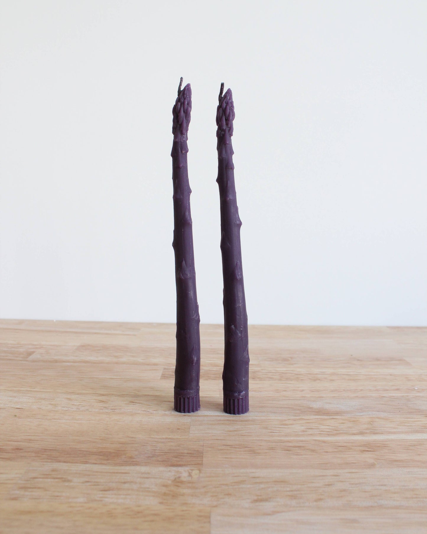Two purple asparagus stalks on a wooden surface with a white background
