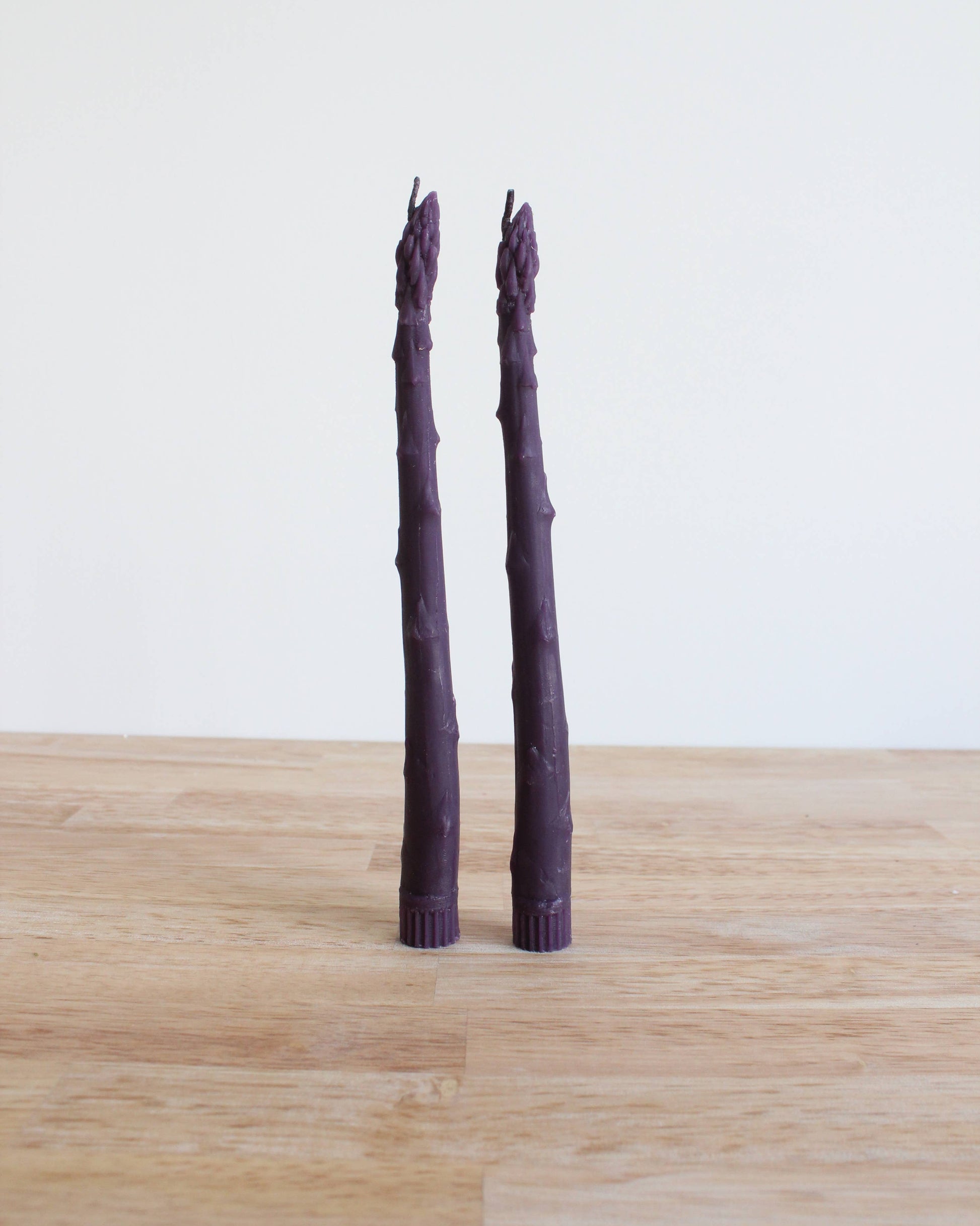 Two purple asparagus stalks on a wooden surface with a white background