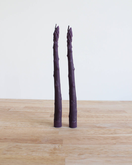 Two purple asparagus stalks on a wooden surface with a white background