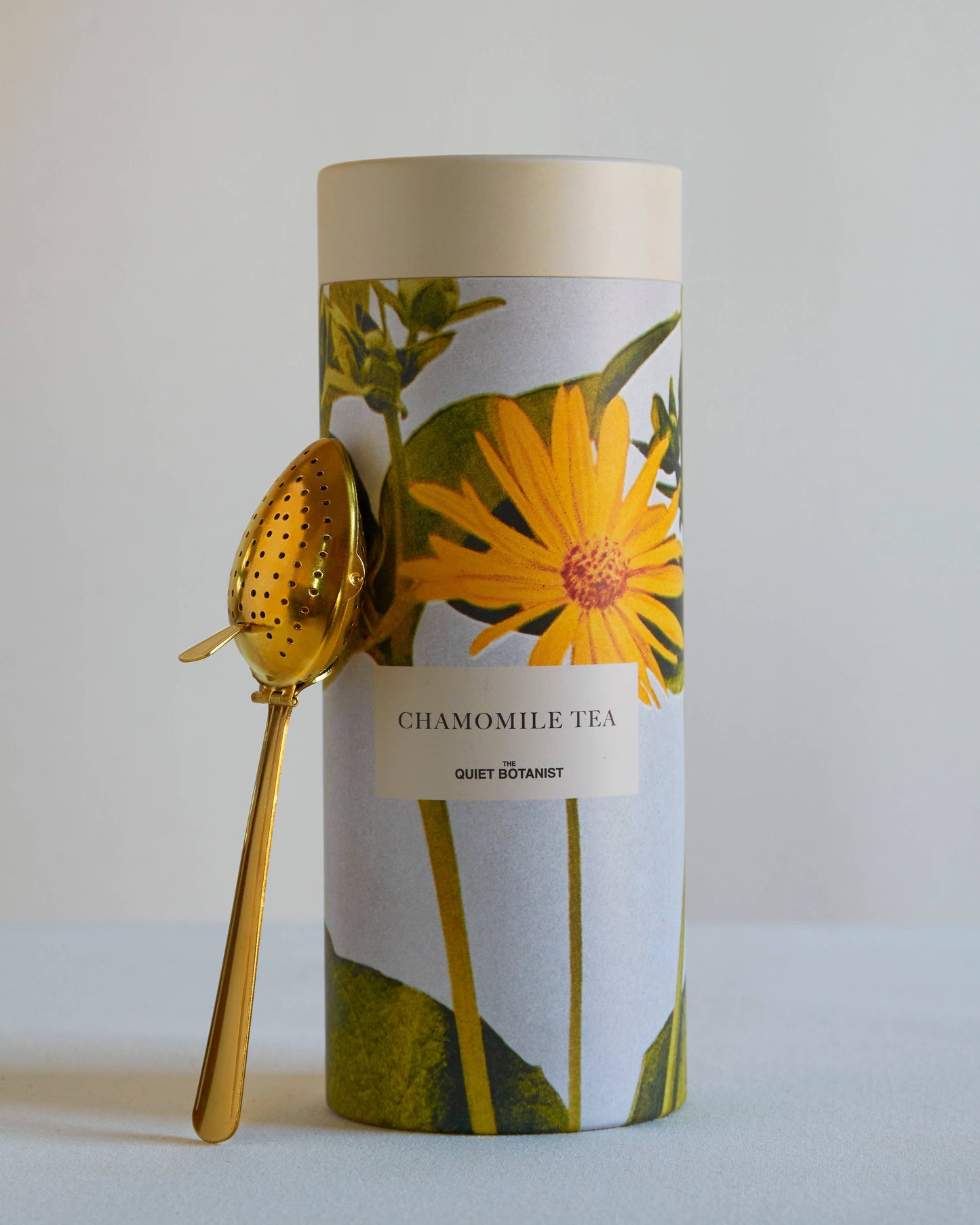 Chamomile tea packaging with a gold spoon on a light gray background
