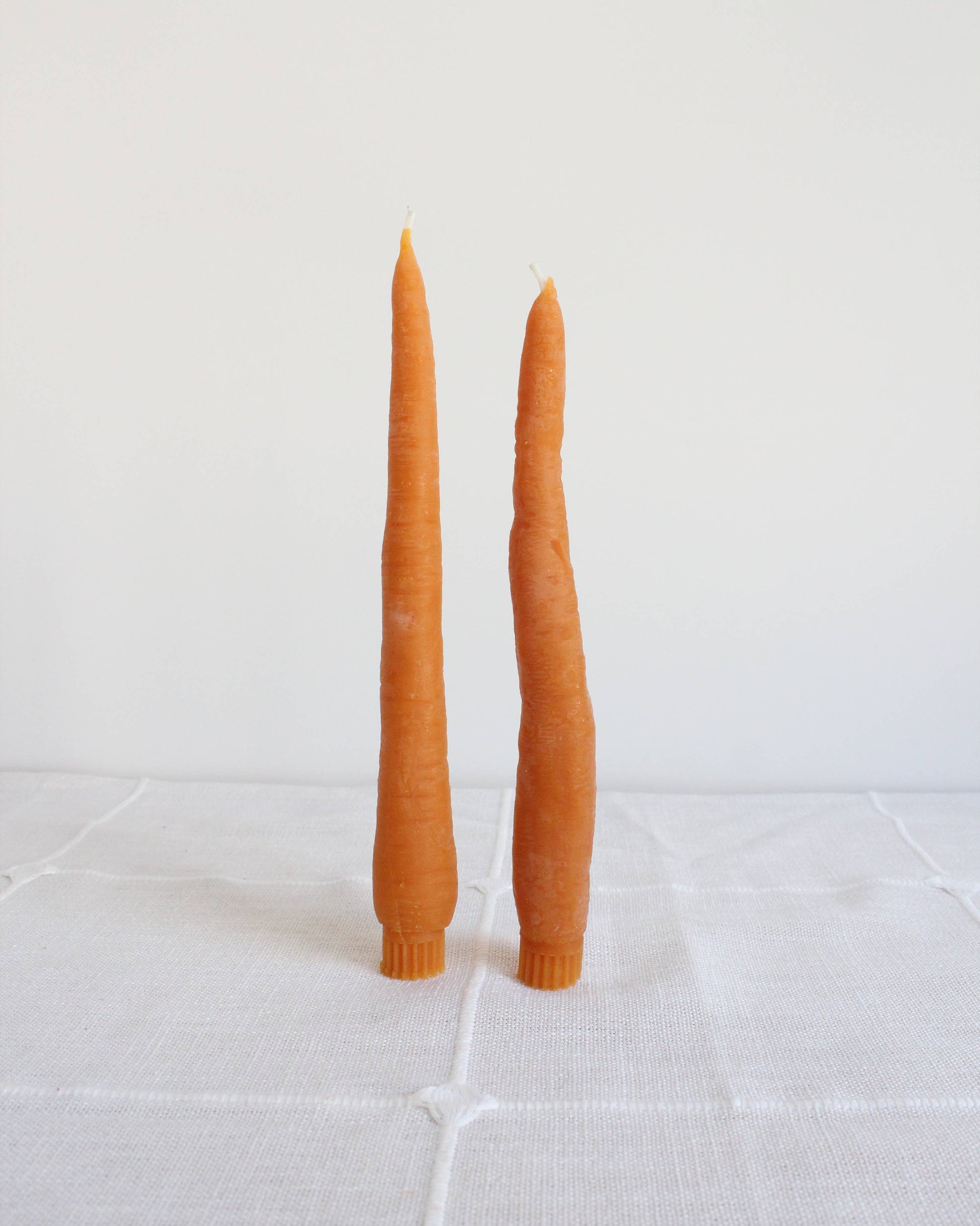 Two orange candles on a white tiled surface
