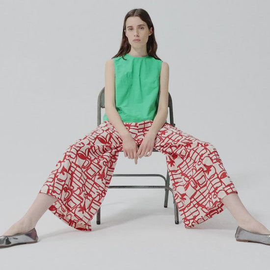 Woman sitting on a chair wearing a green top and red patterned skirt.