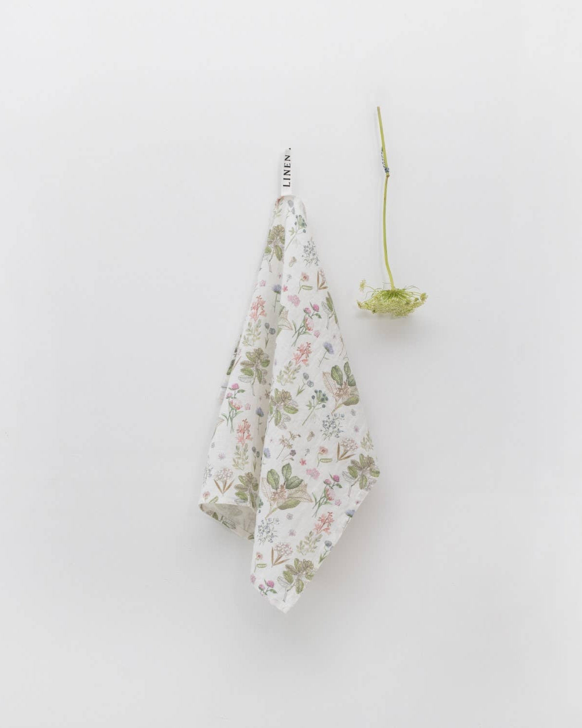 Floral-patterned towel hanging on a white wall with a small plant.