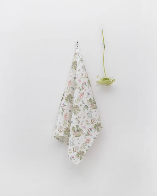 Floral-patterned towel hanging on a white wall with a small plant.