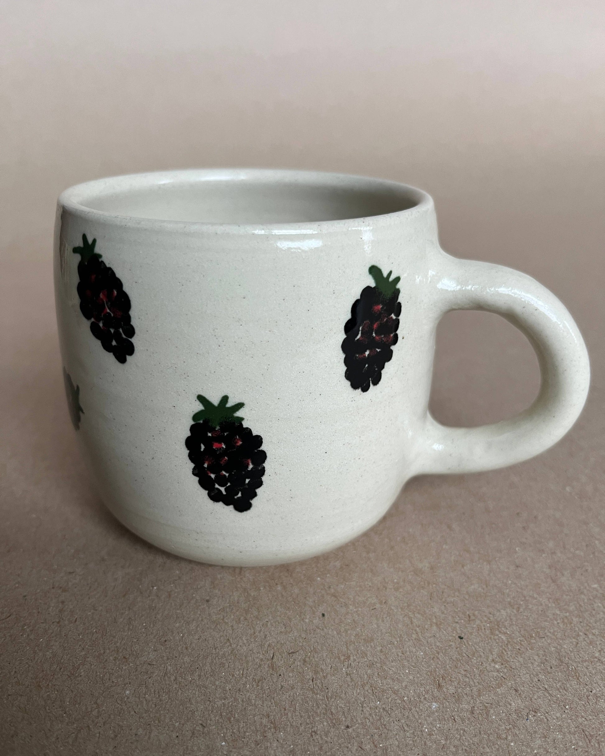 White mug with blackberry designs on a beige background