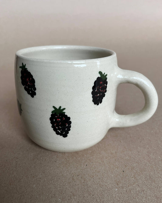 White mug with blackberry designs on a beige background