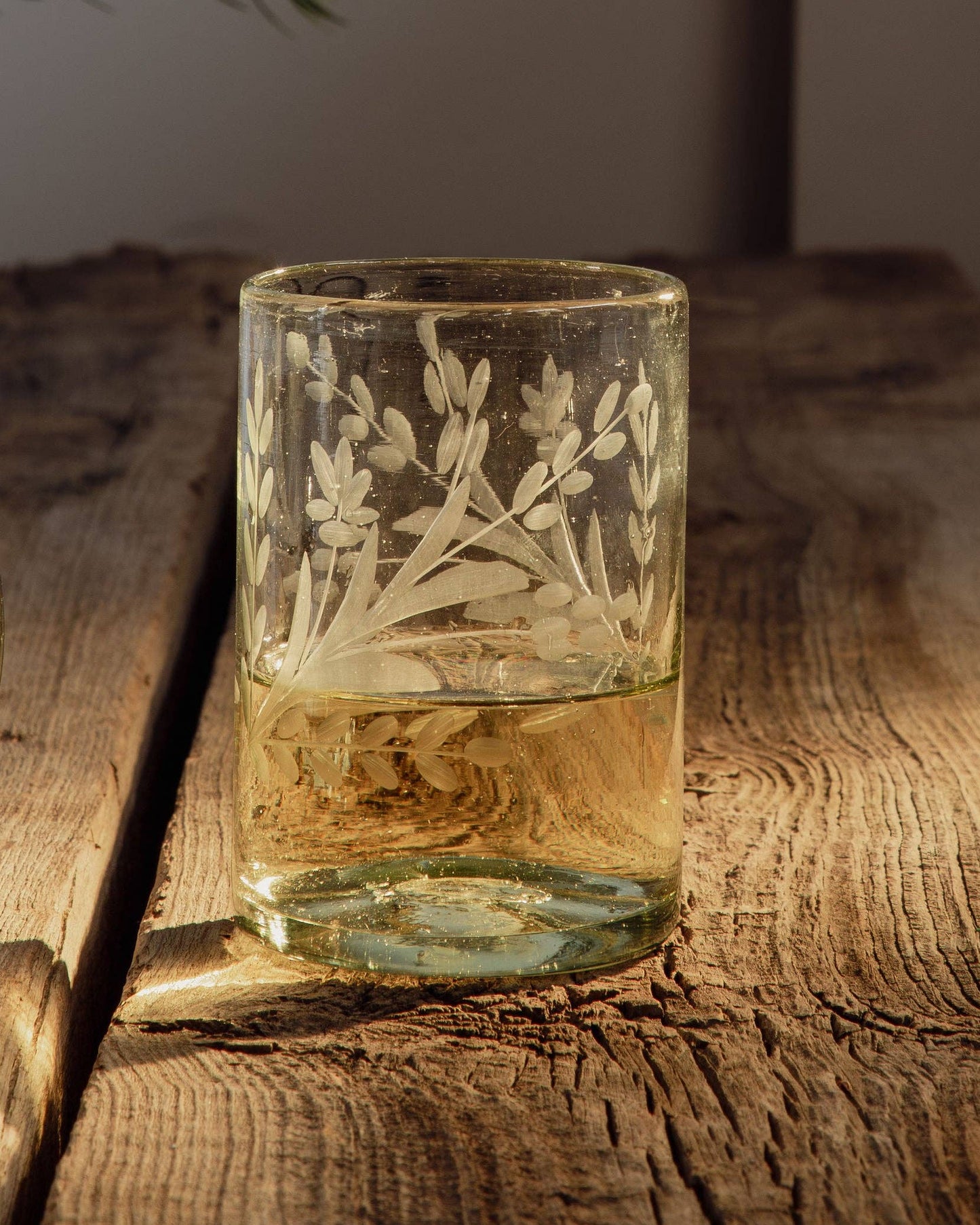 Etched glass candle holder on a wooden surface with a plant in the background
