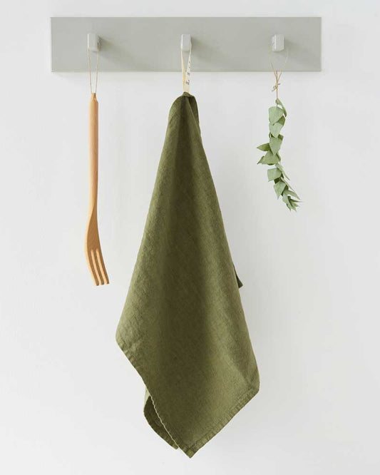 Green towel hanging on a wall hook with a white background