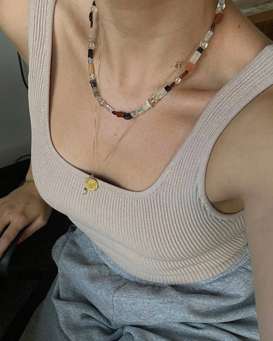 Person wearing a beige tank top with a beaded necklace