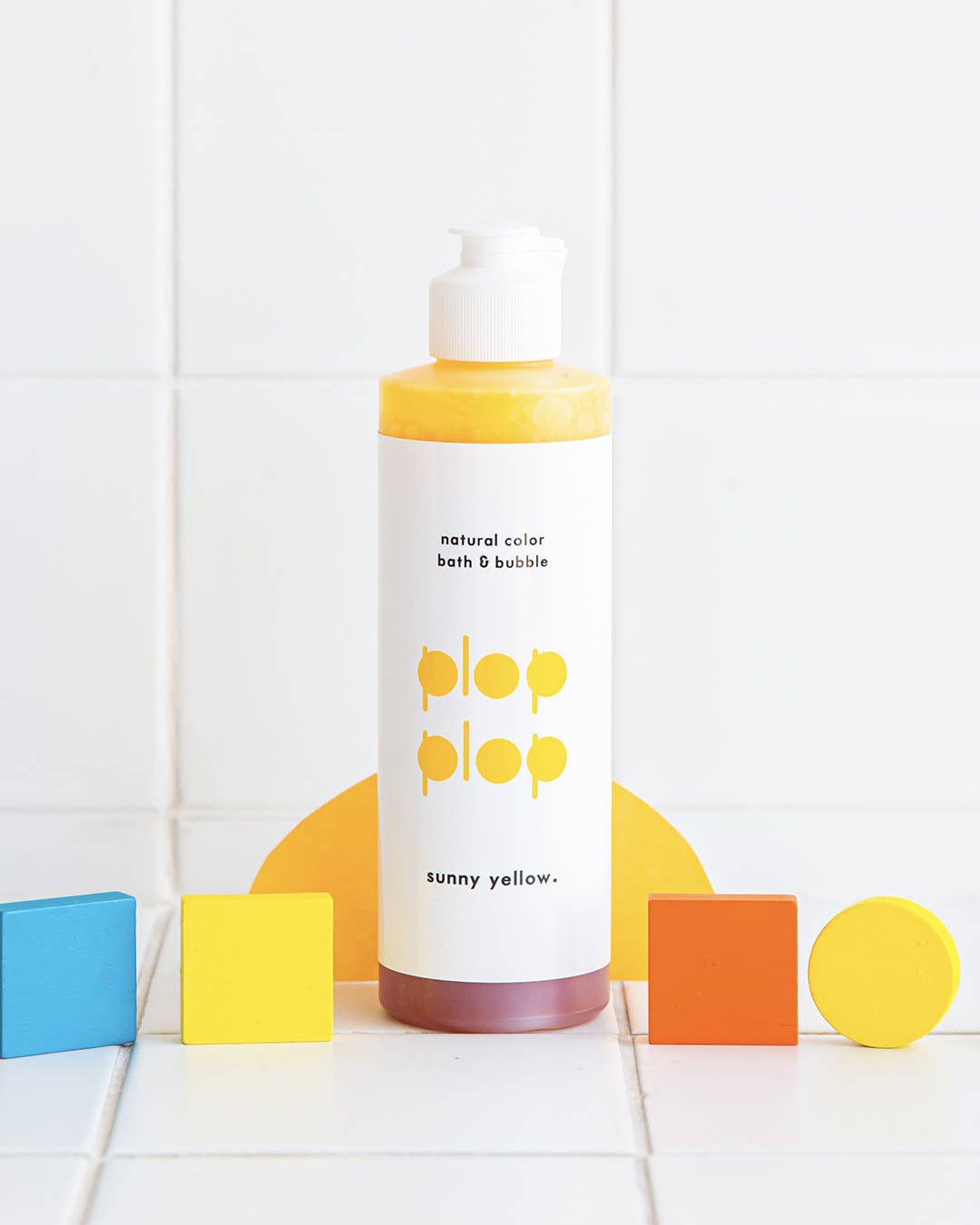 Bottle of 'pop pop' bath and bubble product with colorful geometric shapes on a white tiled background