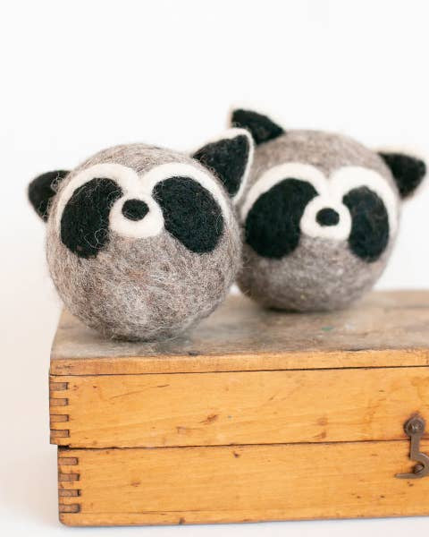 Two felted raccoon toys on a wooden box with a white background