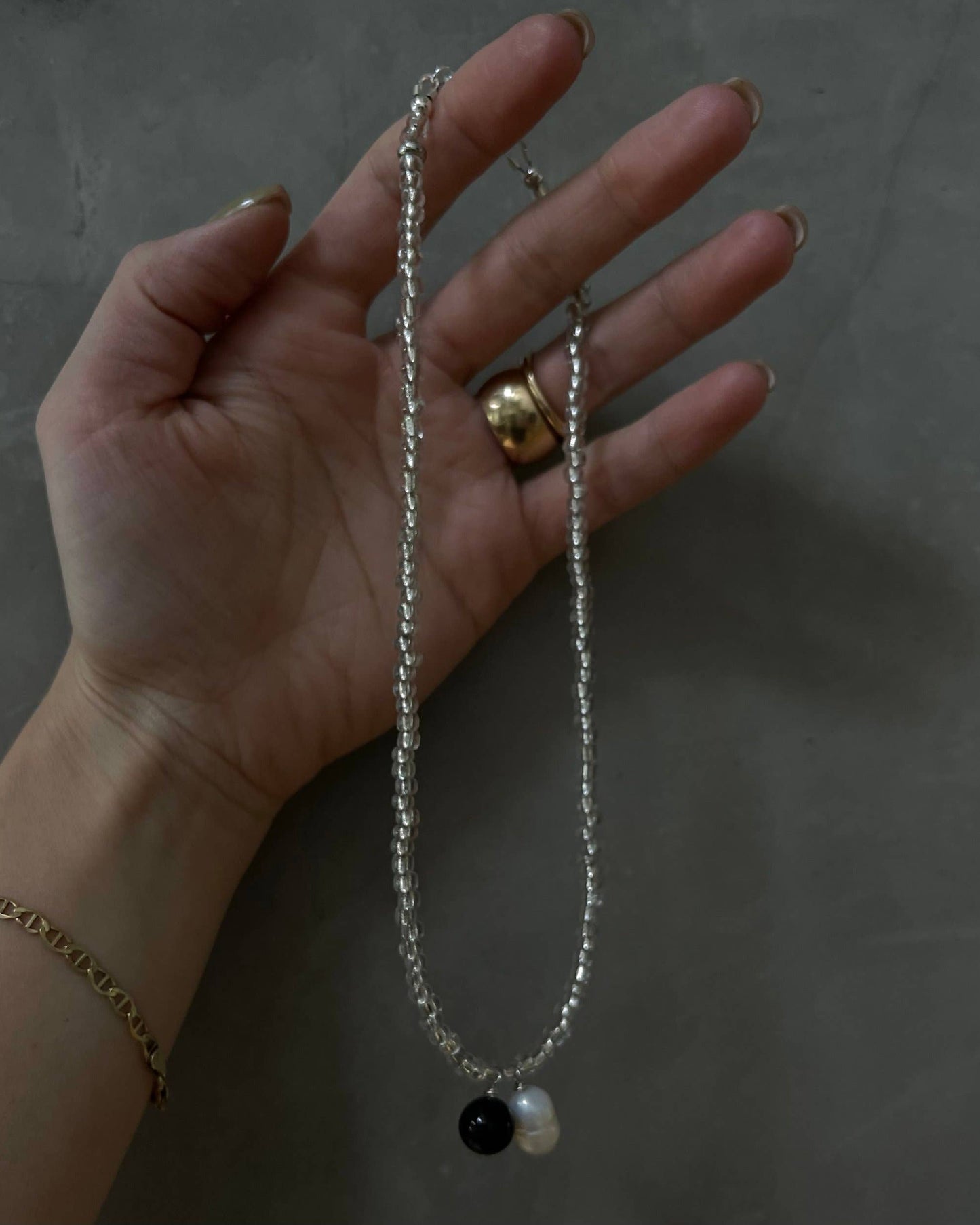 Hand holding a necklace with a black and white pendant against a dark background