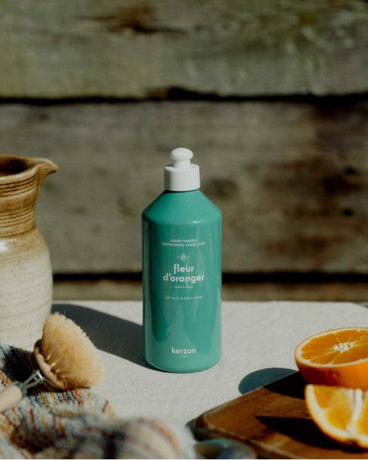 Teal bottle with white pump on a stone surface with oranges and a ceramic pot.