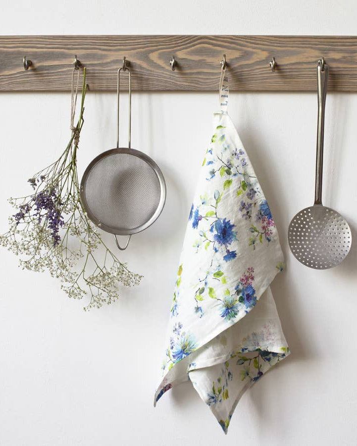 Kitchen utensils and a floral towel hanging on a wooden rack against a white wall.