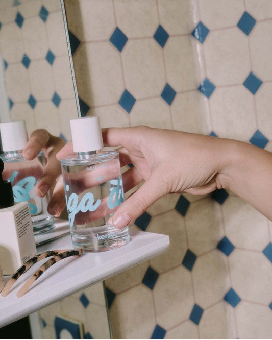 Hand holding a glass bottle labeled 'Keria' against a patterned wall.