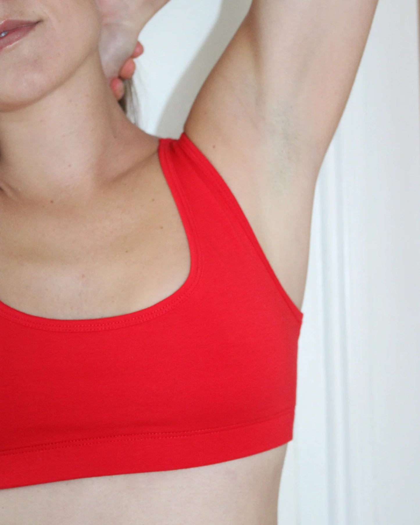Person wearing a red sports bra with a white towel on a plain background