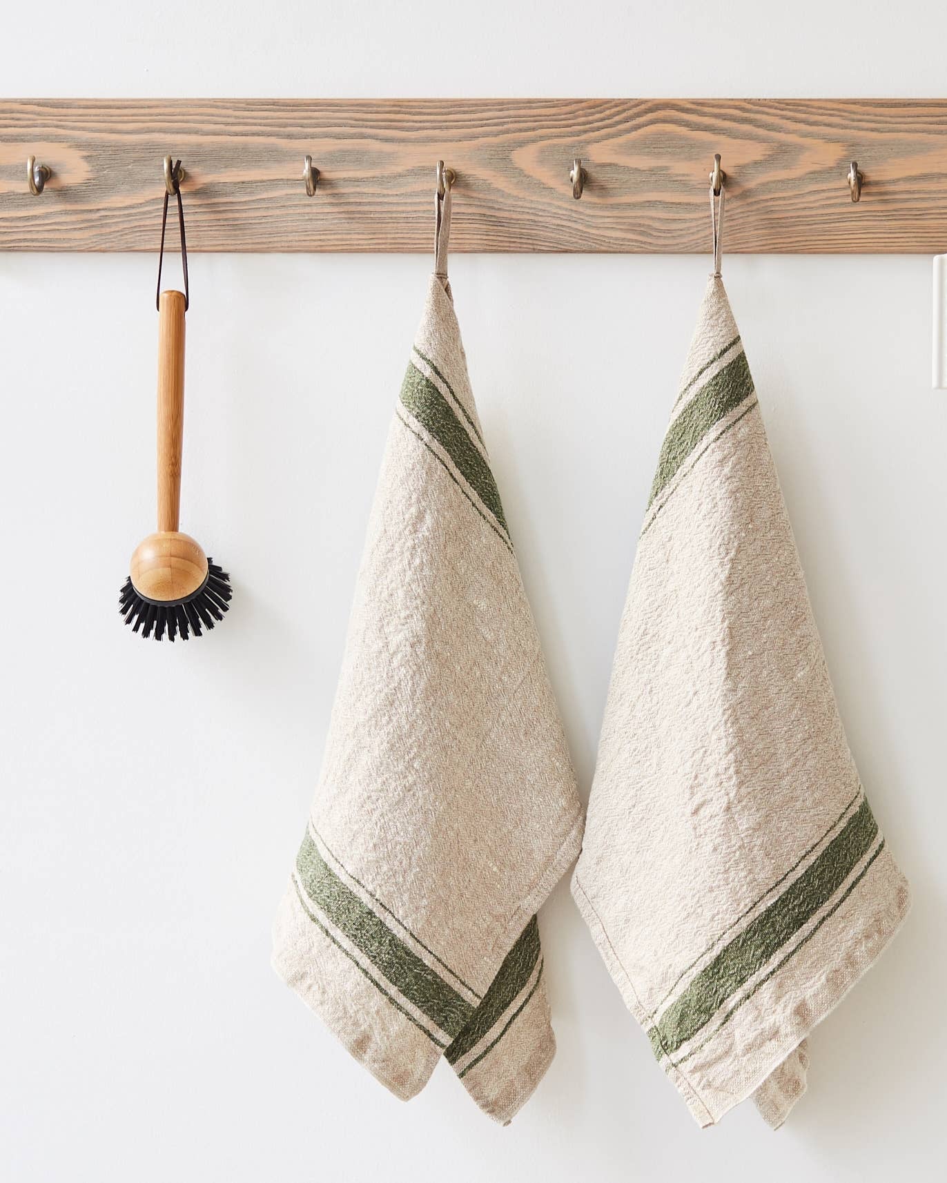Two beige towels with green stripes hanging on a wooden rack against a white wall.