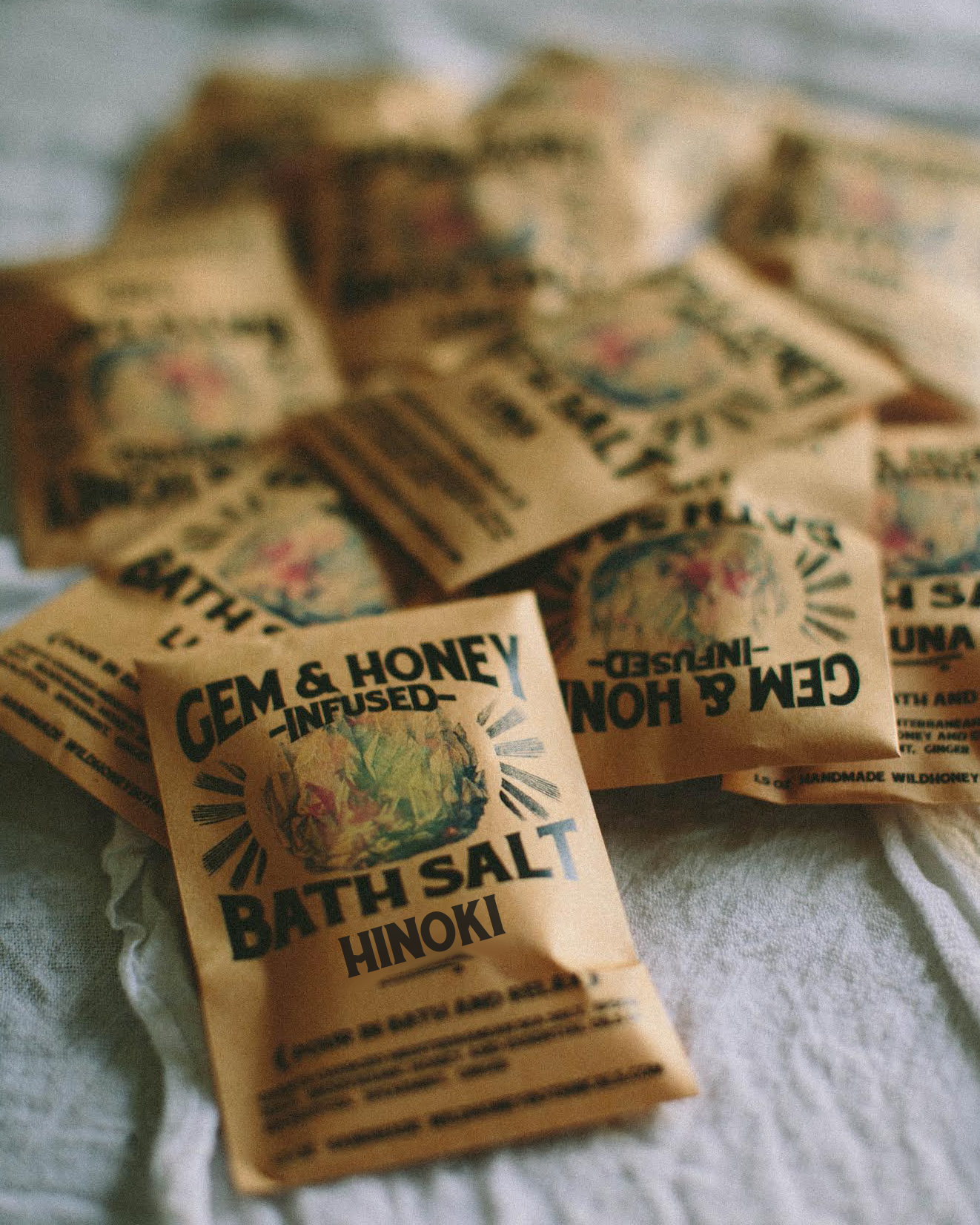 Bath salt packets labeled 'Gem & Honey Infused Bath Salt Hinoki' on a textured surface.