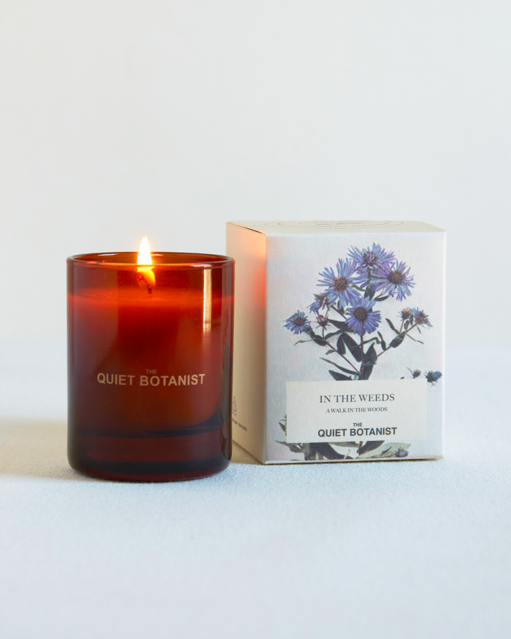 Candle with 'Quiet Botanist' branding next to its packaging on a white background
