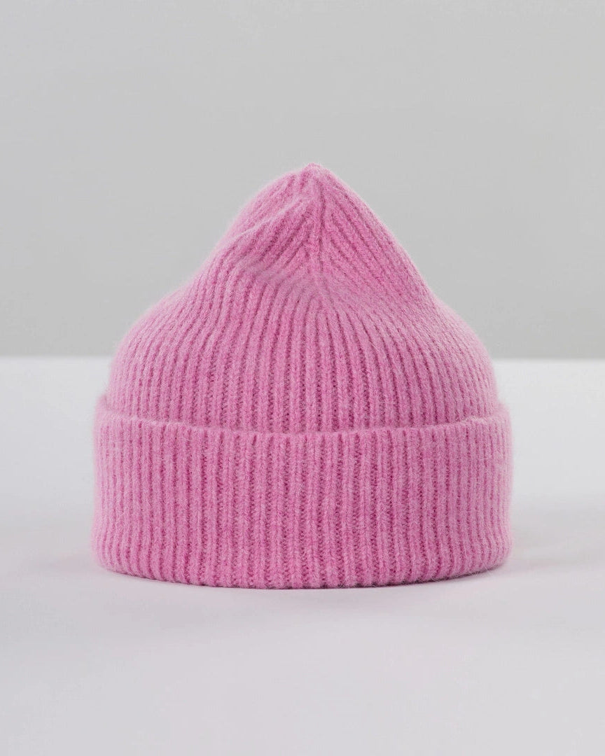 A pink ribbed knit beanie hat with a pointed top and folded cuff, photographed on a clean white surface against a light gray background.