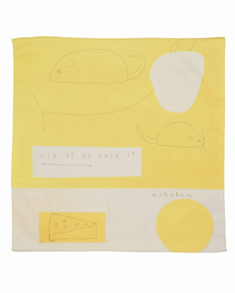 A square yellow and white fabric napkin with minimalist line drawings of a mouse, a slice of cheese, and a yellow circle, featuring the text 'USE IT OR LOSE IT' and the brand name 'mishkin' printed on it.