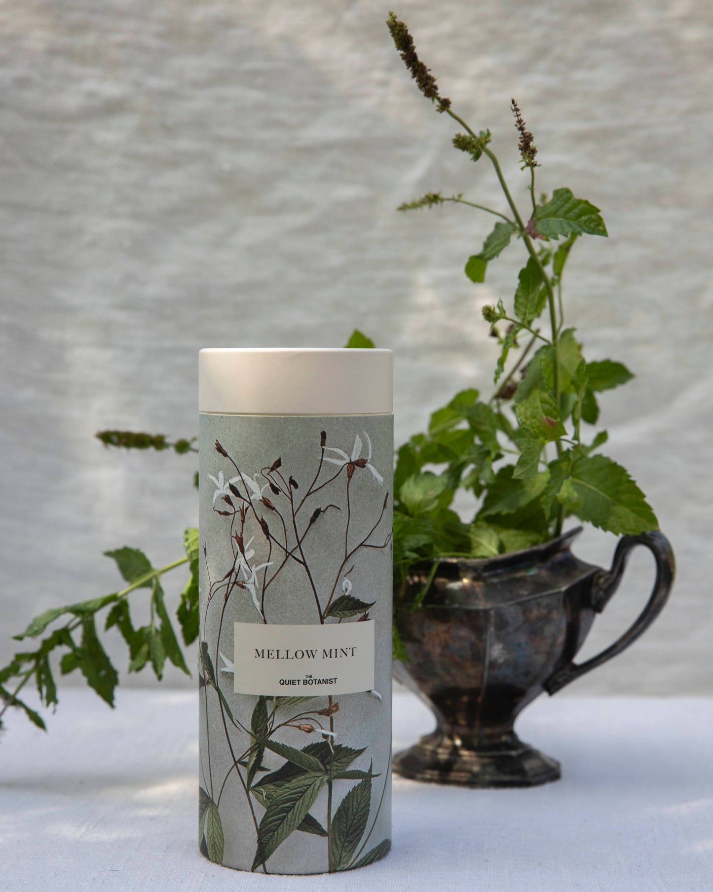 Tea labeled 'Mellow Mint' with botanical design on a white surface with plants in the background