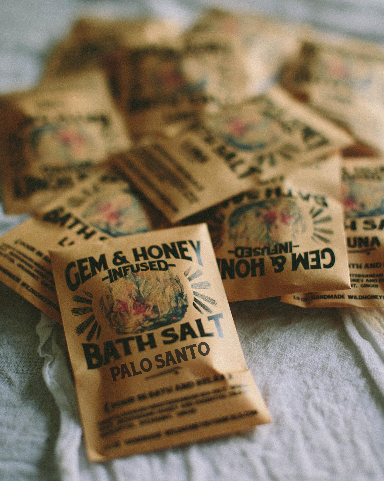 Bath salt packets labeled 'Gem & Honey Infused Bath Salt Hinoki' on a textured surface.